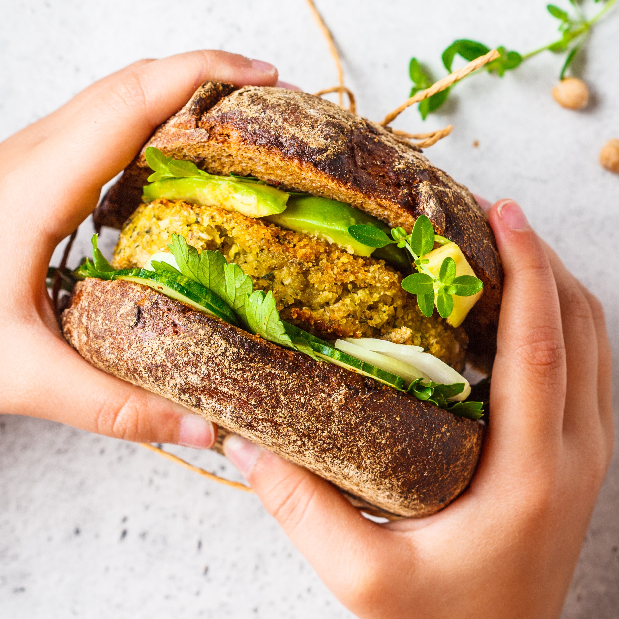 Vegan sandwich with chickpea patty, avocado, cucumber and greens in rye bread in children's hands.